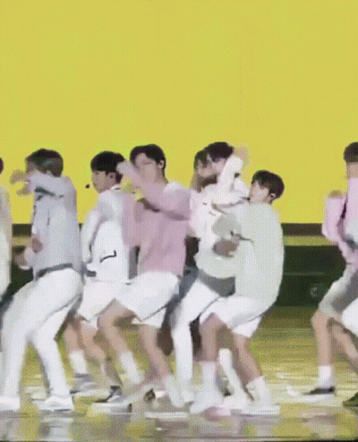 A Group Of People Are Dancing On A Stage In Front Of An Orange Background GIF