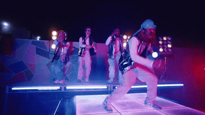 A Group Of People Are Dancing On A Stage With Purple Lights Behind Them GIF
