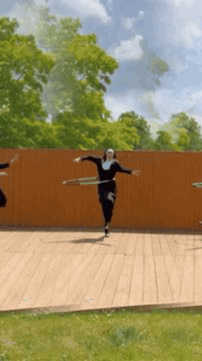 A Group Of People Are Dancing With Hula Hoops On A Wooden Deck . GIF