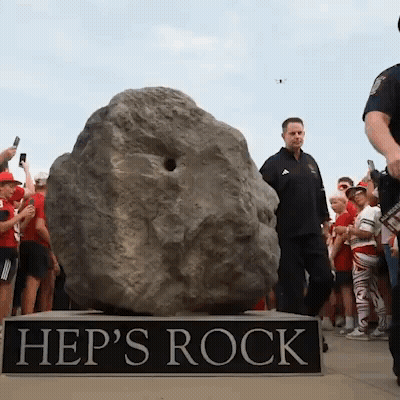 A Group Of People Are Gathered Around A Large Rock Called Hep 'S Rock GIF