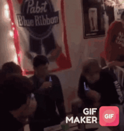 A Group Of People Are Gathered Around A Table With A Pabst Blue Ribbon Banner Behind Them GIF