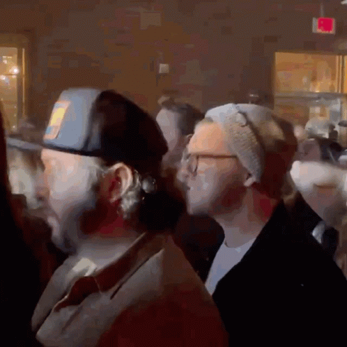 A Group Of People Are Gathered In A Room With A Red Exit Sign In The Background GIF