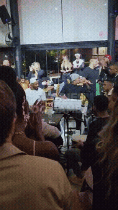 A Group Of People Are Gathered In A Room With A Sign That Says ' One Camp ' In The Corner GIF