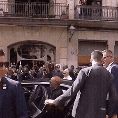 A Group Of People Are Gathered Outside A Building With A Blue Sign On The Wall That Says ' A ' On It GIF