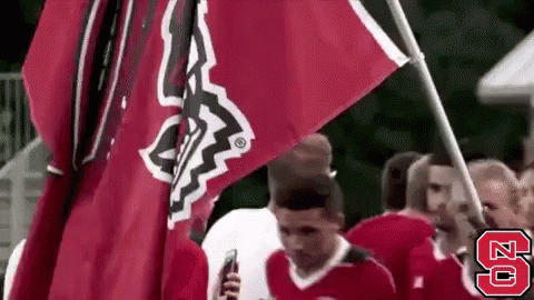 A Group Of People Are Holding A Red Flag And A Man Is Holding A Cell Phone . GIF