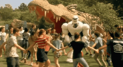 A Group Of People Are Holding Hands In Front Of A Statue Of A Dinosaur And A Robot GIF