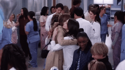 A Group Of People Are Hugging Each Other In A Crowded Room . GIF