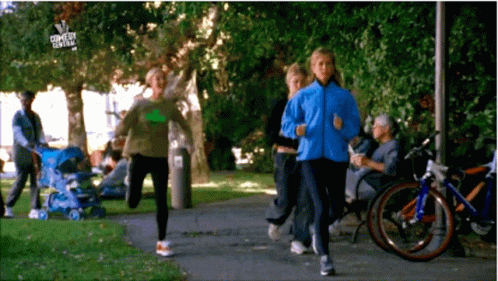A Group Of People Are Jogging In A Park With A Sign That Says Comedy Central On It GIF