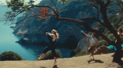 A Group Of People Are Jumping In The Air On A Hill Overlooking A Body Of Water GIF
