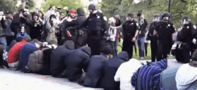 A Group Of People Are Kneeling Down In Front Of A Police Line GIF