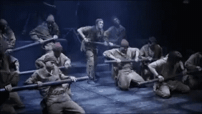 A Group Of People Are Kneeling Down On A Stage Holding Swords . GIF