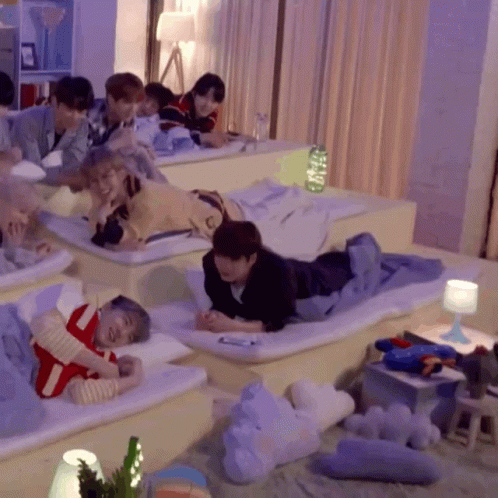 A Group Of People Are Laying On Mattresses In A Room With Purple Curtains GIF