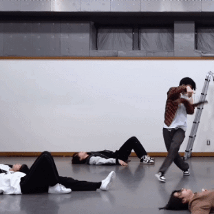 A Group Of People Are Laying On The Floor While A Man Stands Behind Them With A Ladder GIF