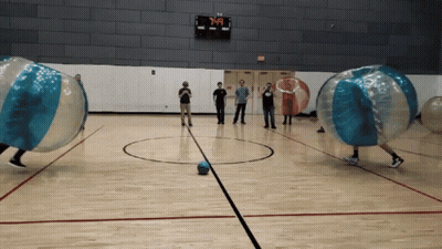 A Group Of People Are Playing A Game Of Bubble Soccer In A Gym With A Scoreboard That Says 7:40 GIF