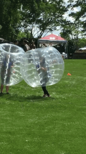 A Group Of People Are Playing Bubble Soccer In A Grassy Field GIF