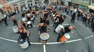 A Group Of People Are Playing Drums On A Street With A Sign That Says ' Rhythm ' GIF