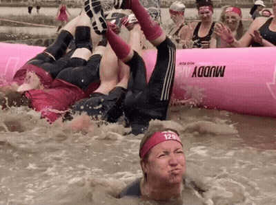 A Group Of People Are Playing In A Muddy Pool With A Pink Raft That Says Muddy On It GIF