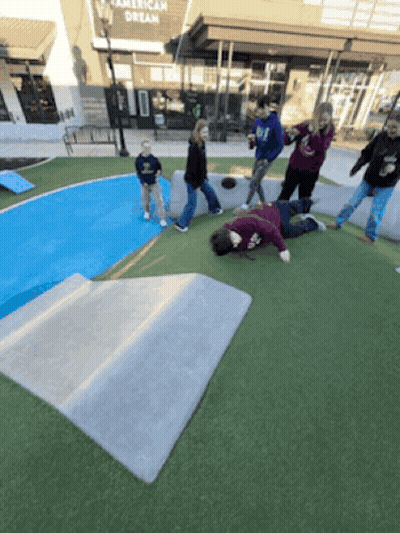 A Group Of People Are Playing In A Park In Front Of An American Dream Store GIF