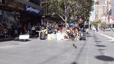A Group Of People Are Playing Instruments On A Sidewalk In Front Of A Sign That Says Souldriver Shop GIF