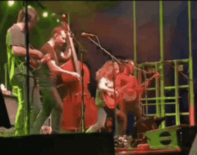A Group Of People Are Playing Instruments On A Stage And Singing Into Microphones . GIF