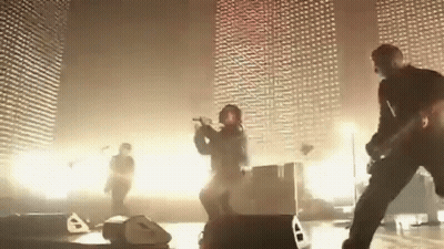 A Group Of People Are Playing Instruments On A Stage In Front Of A Wall . GIF