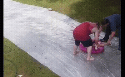 A Group Of People Are Playing On A Water Slide In The Backyard . GIF