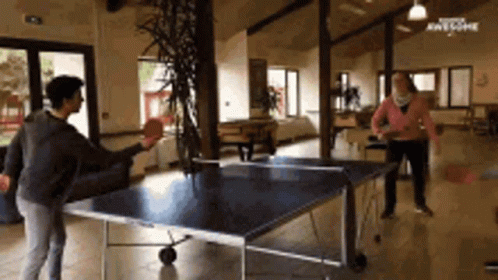 A Group Of People Are Playing Ping Pong In A Room GIF