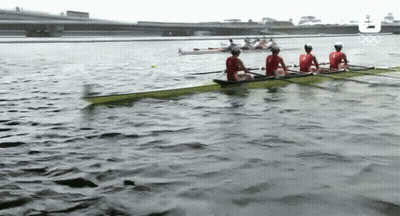 A Group Of People Are Rowing A Boat On A Lake With The Olympic Logo In The Background GIF