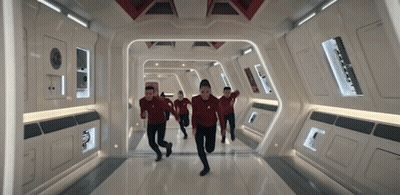 A Group Of People Are Running Down A Hallway In A Spaceship . GIF