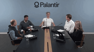 A Group Of People Are Sitting Around A Conference Table With A Palantir Logo Behind Them GIF