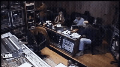 A Group Of People Are Sitting Around A Table In A Recording Studio With A Sign On The Wall That Says ' A ' GIF