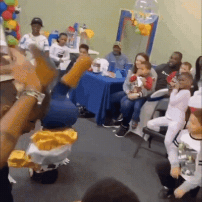 A Group Of People Are Sitting Around A Table In A Room With Balloons . GIF