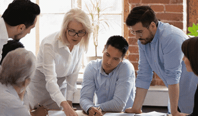 A Group Of People Are Sitting Around A Table Looking At A Piece Of Paper . GIF