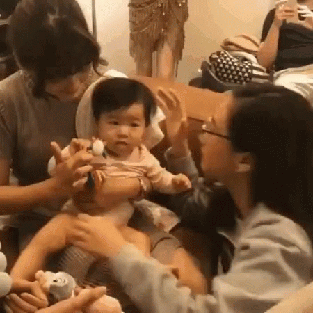 A Group Of People Are Sitting Around A Table With A Baby In Their Lap . GIF