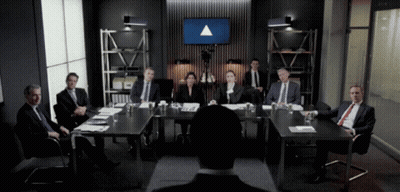 A Group Of People Are Sitting Around A Table With A Large Screen Behind Them That Says ' Triangle ' GIF