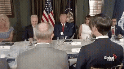 A Group Of People Are Sitting Around A Table With A Man In A Suit . GIF