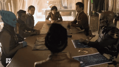 A Group Of People Are Sitting Around A Table With A Tv Logo In The Background GIF