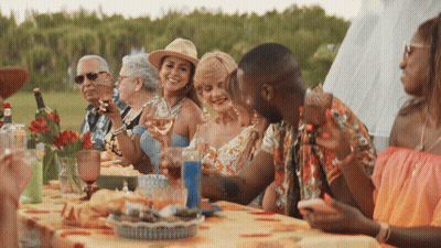 A Group Of People Are Sitting Around A Table With Glasses Of Wine GIF