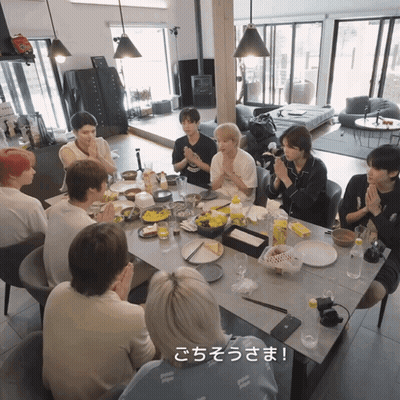 A Group Of People Are Sitting Around A Table With Plates Of Food And A Sign That Says " ごちそうさま " GIF
