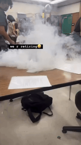 A Group Of People Are Sitting Around A Table With Smoke Coming Out Of It And A Sign That Says We R Retiring GIF
