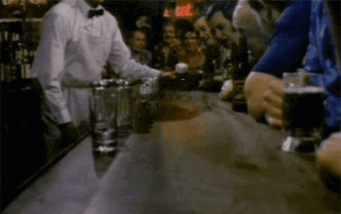 A Group Of People Are Sitting At A Bar With A Man In A Bow Tie Behind Them GIF