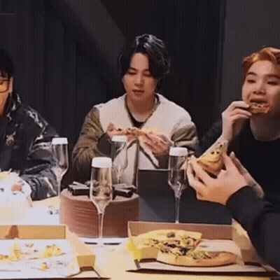A Group Of People Are Sitting At A Table Eating Pizza And Wine Glasses . GIF