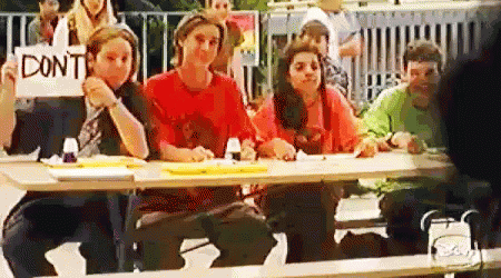 A Group Of People Are Sitting At A Table Holding A Sign That Says `` Don 'T '' . GIF