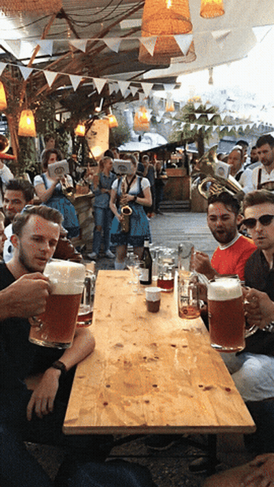 A Group Of People Are Sitting At A Table Holding Mugs Of Beer GIF