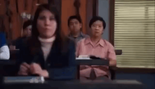 A Group Of People Are Sitting At Desks In A Classroom In Front Of A Window . GIF