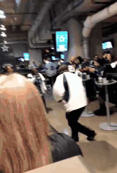 A Group Of People Are Sitting At Tables In A Room With A TV Screen That Says ' NFL ' On It GIF