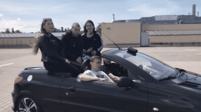 A Group Of People Are Sitting In A Convertible Car With A Man Driving GIF