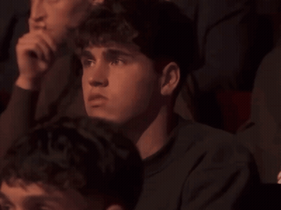 A Group Of People Are Sitting In A Dark Room And One Of Them Is Looking At Something GIF