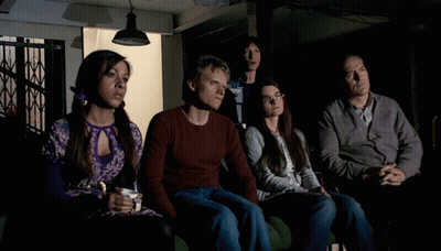 A Group Of People Are Sitting In A Dark Room And One Woman Is Holding A Cup Of Coffee GIF