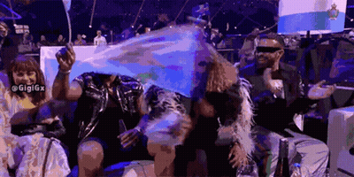 A Group Of People Are Sitting In A Stadium Holding Flags And One Of Them Is Wearing Sunglasses GIF
